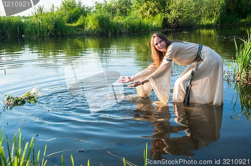 Image of Attractive funny girl lowers wreath in water