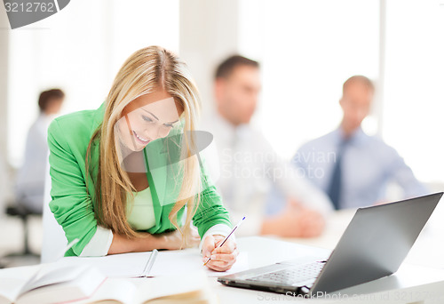 Image of attractive businesswoman taking notes in office