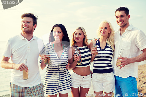 Image of smiling friends with drinks in bottles on beach