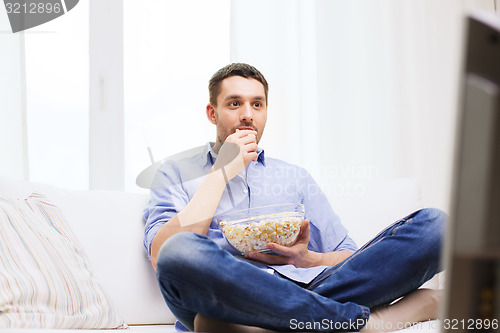 Image of young man watching tv and eating popcorn at home
