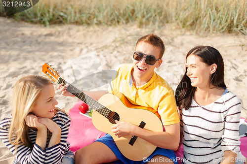 Image of group of happy friends playing guitar on beach