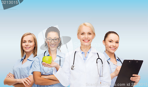 Image of smiling female doctor and nurses with green apple
