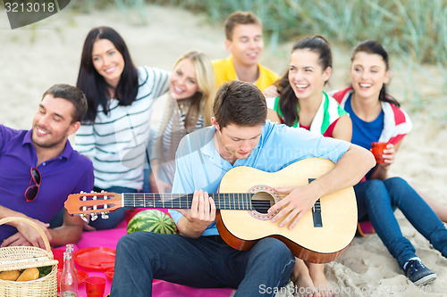 Image of group of happy friends playing guitar on beach