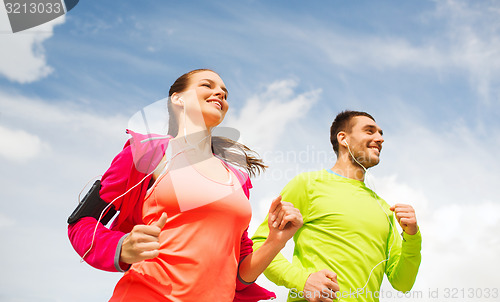 Image of smiling couple with earphones running outdoors