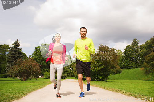 Image of smiling couple with earphones running outdoors