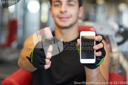 Image of young man with smartphone showing thumbs up in gym