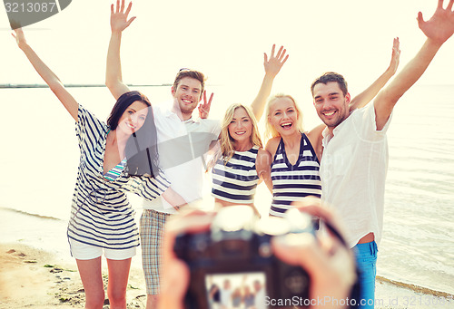 Image of friends on beach waving hands and photographing