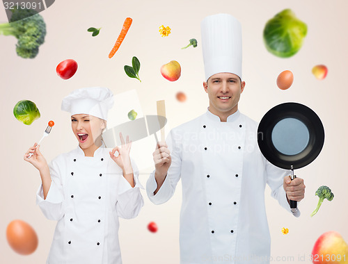 Image of happy male chef holding frying pan and spatula