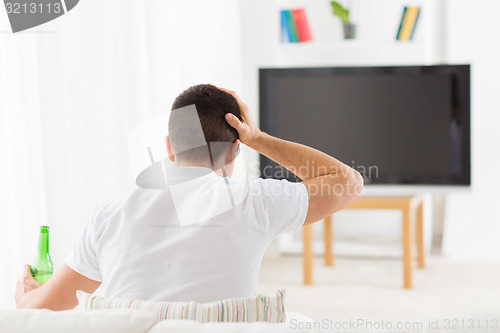 Image of man watching tv and drinking beer at home