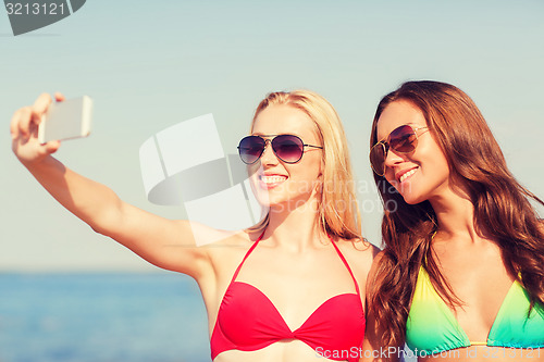 Image of two smiling women making selfie on beach