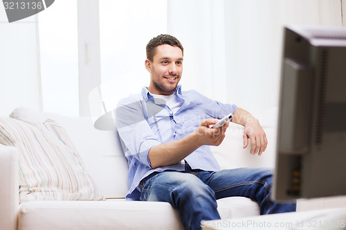 Image of smiling man with tv remote control at home