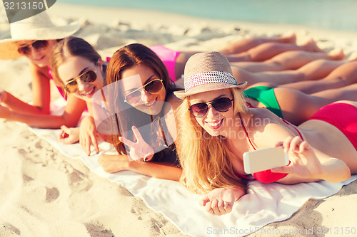 Image of group of smiling women with smartphone on beach