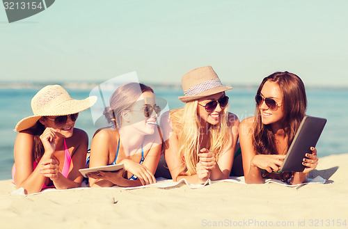Image of group of smiling young women with tablets on beach