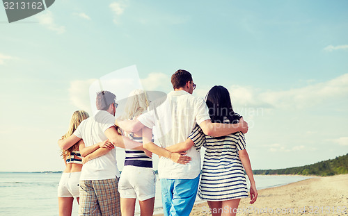 Image of smiling friends hugging and walking on beach