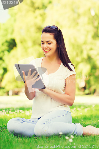 Image of smiling young girl with tablet pc sitting on grass