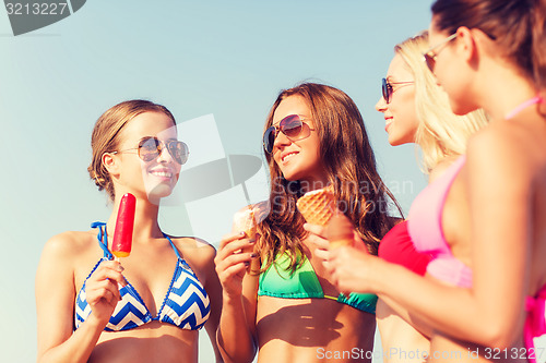 Image of group of smiling women eating ice cream on beach