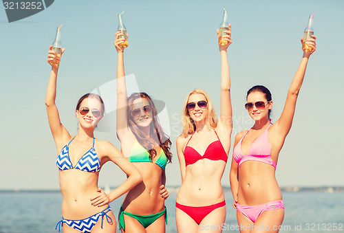 Image of group of smiling young women drinking on beach