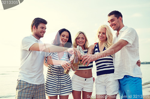 Image of smiling friends clinking bottles on beach