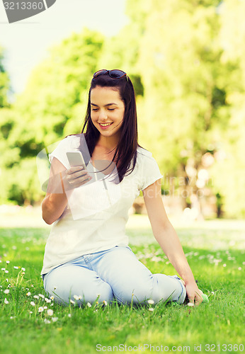 Image of smiling young girl with smartphone sitting in park