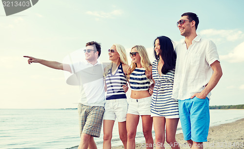 Image of smiling friends in sunglasses walking on beach