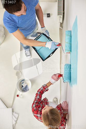 Image of couple with paint rollers painting wall at home