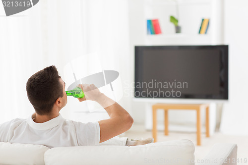 Image of man watching tv and drinking beer at home