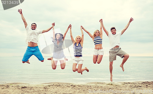 Image of smiling friends in sunglasses walking on beach