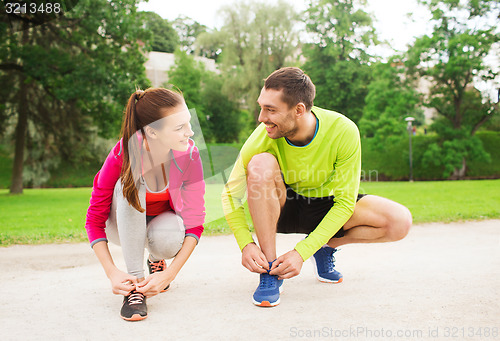 Image of smiling couple tying shoelaces outdoors