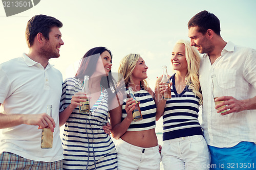 Image of smiling friends with drinks in bottles on beach