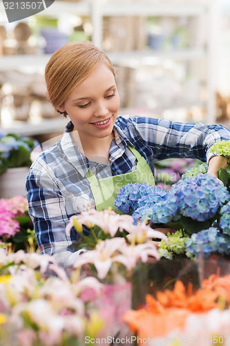 Image of happy woman taking care of flowers in greenhouse