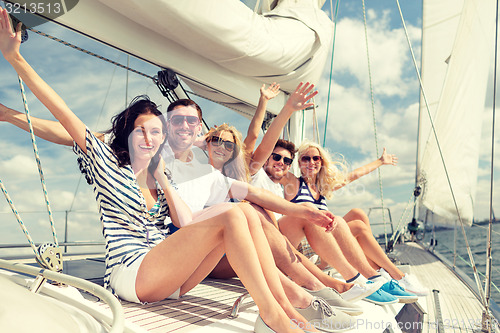 Image of smiling friends sitting on yacht deck and greeting