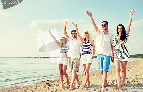 Image of smiling friends walking on beach and waving hands