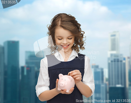 Image of happy girl putting coin into piggy bank