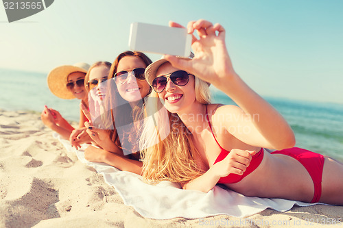 Image of group of smiling women with smartphone on beach