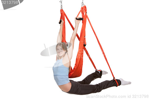 Image of Young woman doing anti-gravity aerial yoga in  red hammock on a seamless white background.