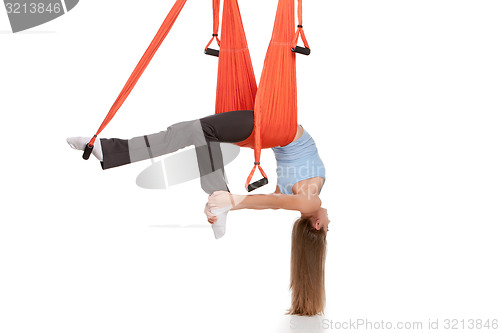 Image of Young woman doing anti-gravity aerial yoga in hammock on a seamless white background.