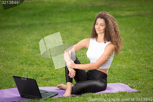 Image of Sporty young woman sitting on the grass with laptop