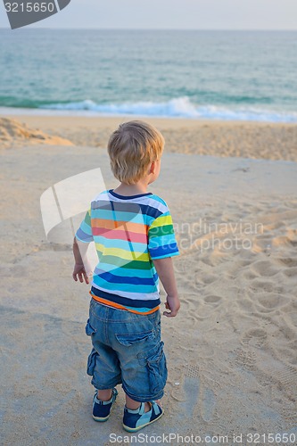 Image of Little boy standing on the beach on sunset