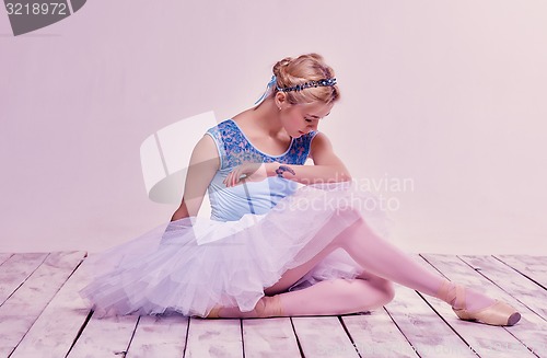 Image of Tired ballet dancer sitting on the wooden floor 