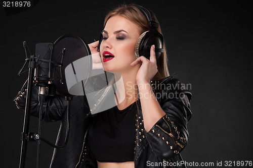 Image of Portrait of a beautiful woman singing into microphone with headphones in studio on black background