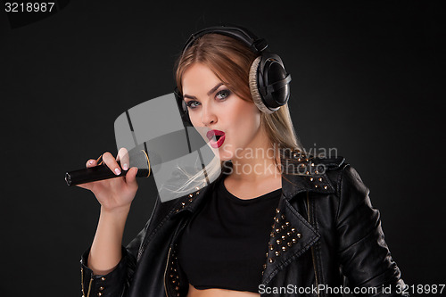 Image of Portrait of a beautiful woman singing into microphone with headphones in studio on black background