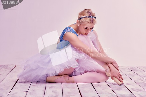 Image of Tired ballet dancer sitting on the wooden floor 