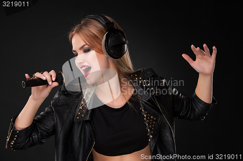 Image of Portrait of a beautiful woman singing into microphone with headphones in studio on black background