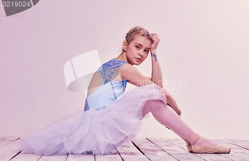 Image of Tired ballet dancer sitting on the wooden floor 