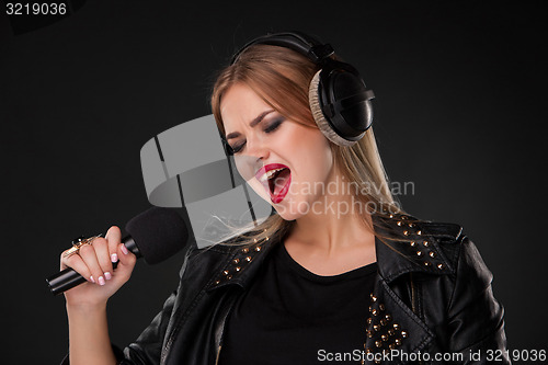 Image of Portrait of a beautiful woman singing into microphone with headphones in studio on black background