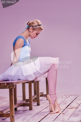 Image of Tired ballet dancer sitting on the wooden floor 