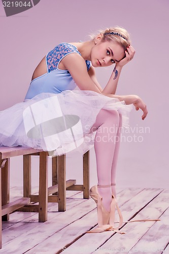 Image of Tired ballet dancer sitting on the wooden floor 