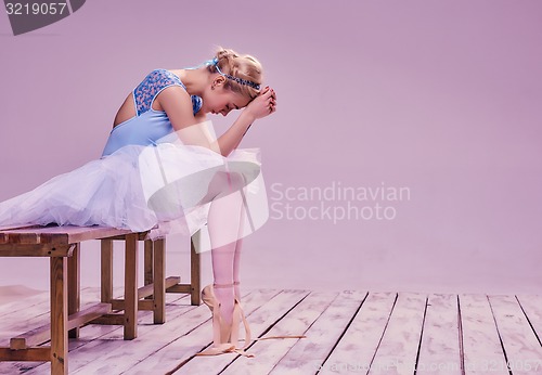 Image of Tired ballet dancer sitting on the wooden floor 