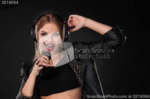 Image of Portrait of a beautiful woman singing into microphone with headphones in studio on black background