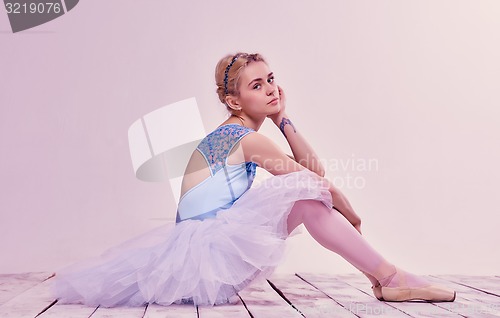 Image of Tired ballet dancer sitting on the wooden floor 